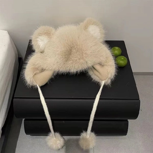 Detailansicht der flauschigen Bärenohren-Mütze in Beige mit dekorativen Bommelbändern