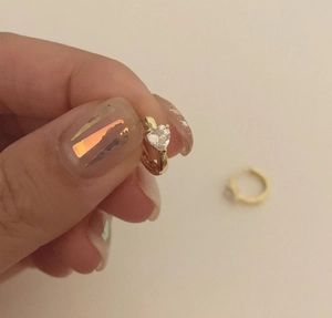 Detail of gold heart-shaped hoop earring with a clear cubic zirconia stone