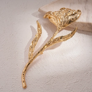 Detailed view of a golden metallic flower brooch with textured petals on a marble base