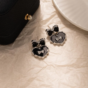 Détail de boucles d'oreilles nœud argenté et cœur noir sur fond en papier texturé