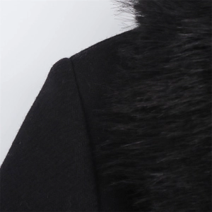 Détail du manteau en laine noire montrant les coutures et la texture du col en fausse fourrure