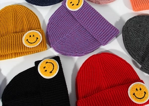 Flat lay detail of colorful ribbed knit beanies with yellow smiley face patches