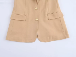 Detail of camel blazer showing gold buttons, flap pockets and twill fabric texture