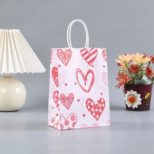 Pink kraft paper gift bag with red hearts and white paper handles for Valentine's Day
