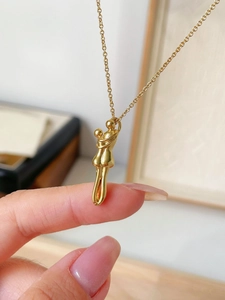 Macro shot of gold-plated abstract hugging figures pendant necklace on a finger