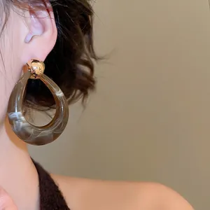 Brown marble resin waterdrop hoop earrings with gold metal stud on model's ear