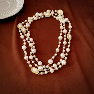 Detail of layered pearl necklace with golden oval clasp on dark brown silk background