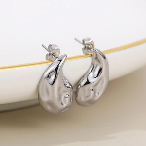 Macro shot of silver teardrop hollow earrings with textured molten metal finish on a ceramic plate