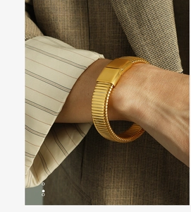 Detail shot of a chunky gold metal tubogas bracelet styled with a brown plaid blazer