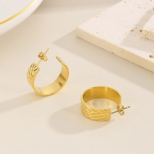 Close-up of wide gold C-shape hoop earrings with snake skin texture on stone background
