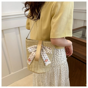 Detailed view of beige woven bucket bag with floral scarf and chain strap on a model
