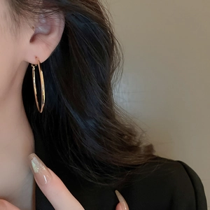 Detailed view of model wearing large golden geometric hoop earrings in a minimalist style