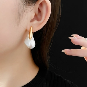 Macro side view of gold-plated earrings with irregular faux pearl drops on a model