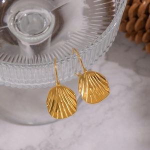 Macro detail of gold shell earrings hanging on textured glass with a natural background