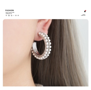 Macro view of C-shaped silver earrings featuring multiple rows of inlaid white pearls