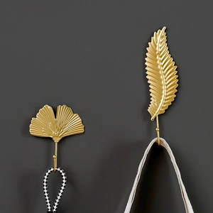 Nordic golden metal leaf wall hooks in ginkgo and feather shapes on a dark background
