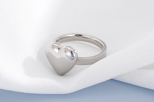 Vue macro d'une bague coeur en argent poli sur tissu blanc avec finition miroir éclatante