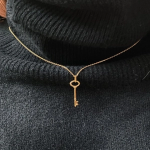 Detailed view of a golden key pendant necklace worn over a black turtleneck sweater