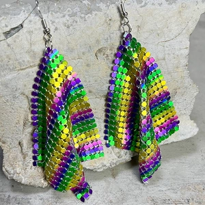 Detail view of rainbow iridescent twisted metal mesh earrings on a rocky texture background