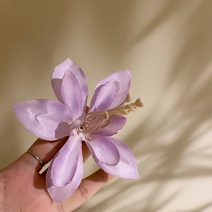 Detailed view of a purple fabric hibiscus hair clip with realistic stamens held in hand