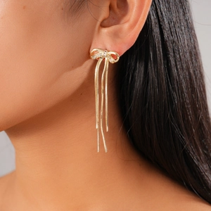 Close-up of elegant 18K gold plated bow earrings with dangling tassels on a female model