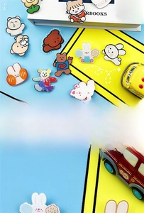 Cute acrylic cartoon bear and rabbit pins displayed on vibrant blue and yellow books