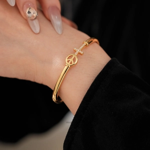 Macro shot of gold-plated bangle featuring a peace sign and crystal-encrusted cross detail