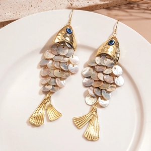 Detailed shot of golden fish earrings with iridescent shell scales on a ceramic tray
