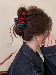 Detail view of large wavy hair claw clip with colorful resin contrast and red ball decor
