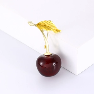 Détail d'une broche cerise rouge foncé avec feuilles dorées sur socles blancs