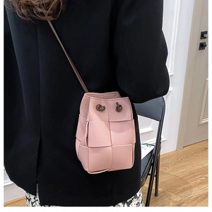 Pink hand-woven PU leather bucket bag with drawstring shown on a model in a casual setting