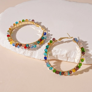 Detail of gold hoop earrings with multi-colored glass beads on a white textured stone