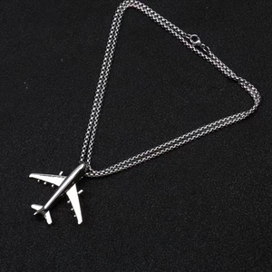 Macro shot of silver airplane pendant necklace with metallic chain on black background