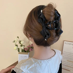 Detail of a black ribbon bow hair claw clip with rhinestones in a French hair bun