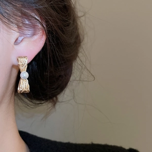 Dettaglio di un orecchino a fiocco dorato con perla indossato da una modella reale
