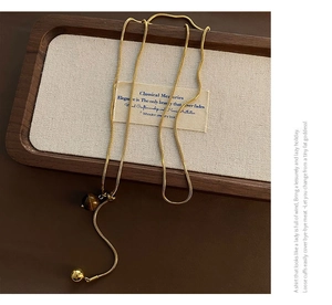 Détail du collier long en Y doré avec perles œil de tigre sur un support en bois élégant