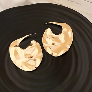 Detailed view of golden hammered geometric earrings with ripple texture on dark plate
