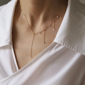 Close-up of gold-plated tassel necklace with sparkling zircon charms on a V-neck shirt
