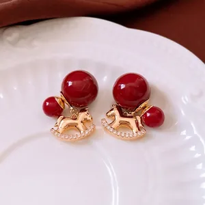 18K gold-plated rocking horse drop earrings with red beads on a ceramic plate