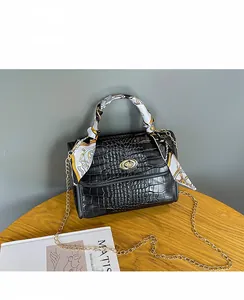 Close-up of black crocodile pattern crossbody bag with silk scarf handle and gold lock