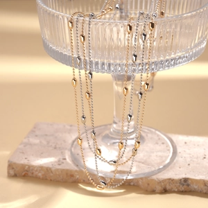 Minimalist metallic rice bead necklaces in gold and silver hanging on a glass