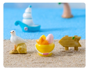 Miniature beach scene with resin seagull, yellow bucket, and wooden sign on real sand