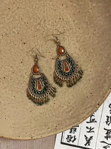 Détail macro de boucles d'oreilles vintage avec pierres orange et pompons métalliques