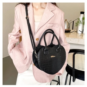 Sac à main cœur noir motif crocodile porté en bandoulière par un mannequin chic