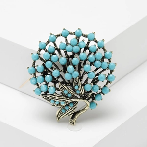 Vintage bronze brooch with turquoise beads in a floral tree design on a white pedestal
