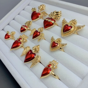 Detailed view of adjustable gold plated rings with red heart wings on white velvet