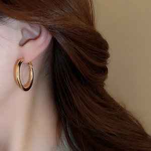 Close-up of polished gold hoop earring worn by a model against a warm beige background