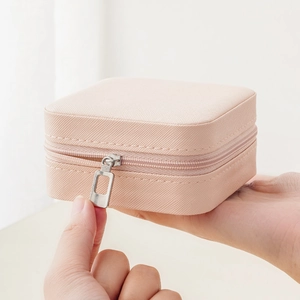 Portable pink square jewelry box with zipper held in hand to show compact travel size