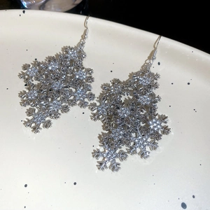Close-up of silver snowflake tassel earrings with sparkling rhinestones on ceramic tray