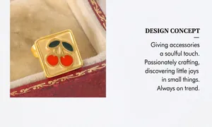 Détail d'une bague carrée dorée avec motif cerise en émail dans un écrin de velours